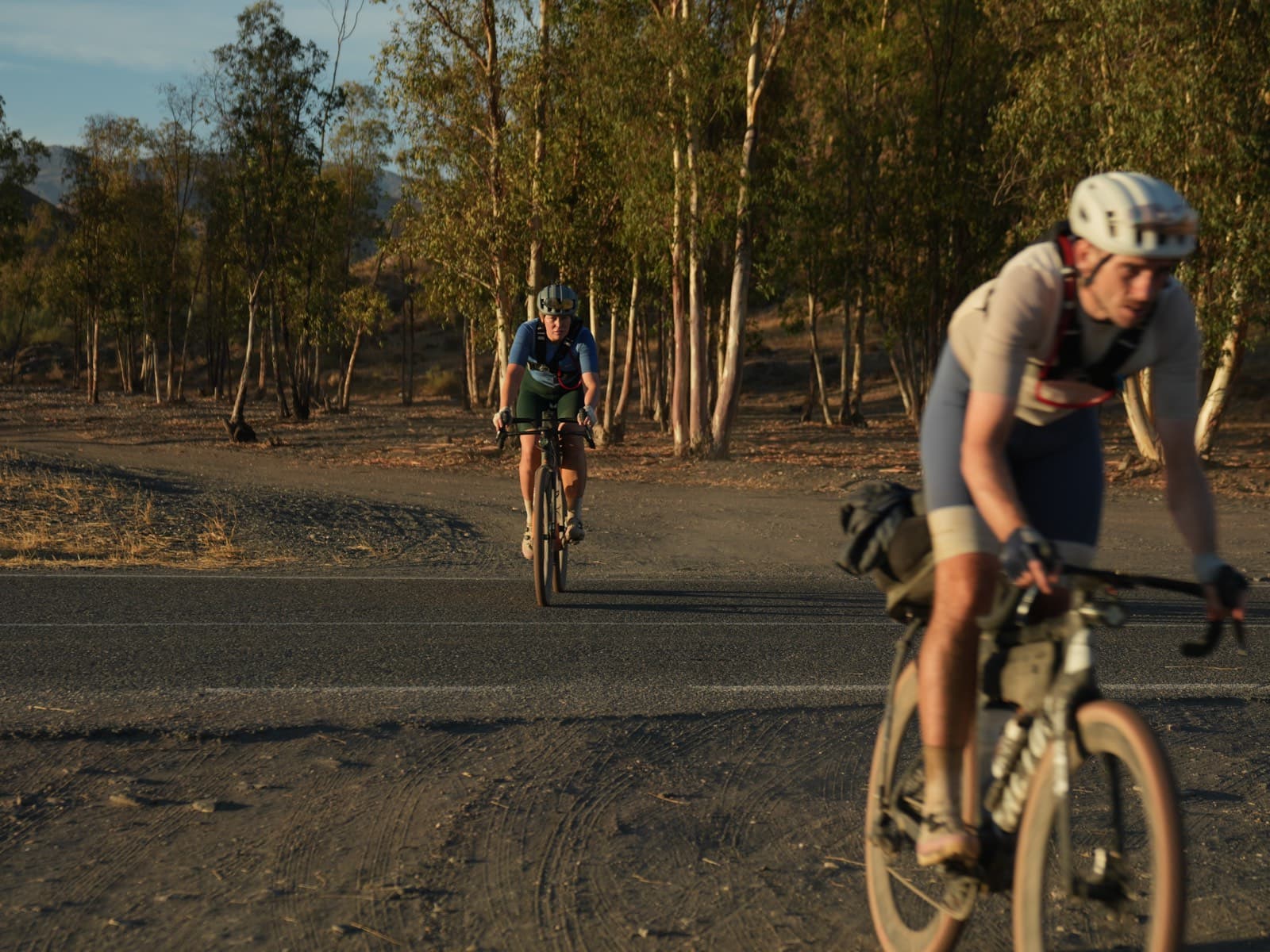 Two cyclists riding through golden hour light in a birch forest